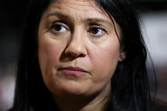 Close-up of a dark-haired person looking forward with a serious expression against a blurred background.