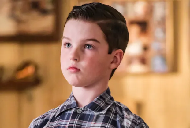 A young boy in a plaid shirt looks upward against a softly blurred indoor background.